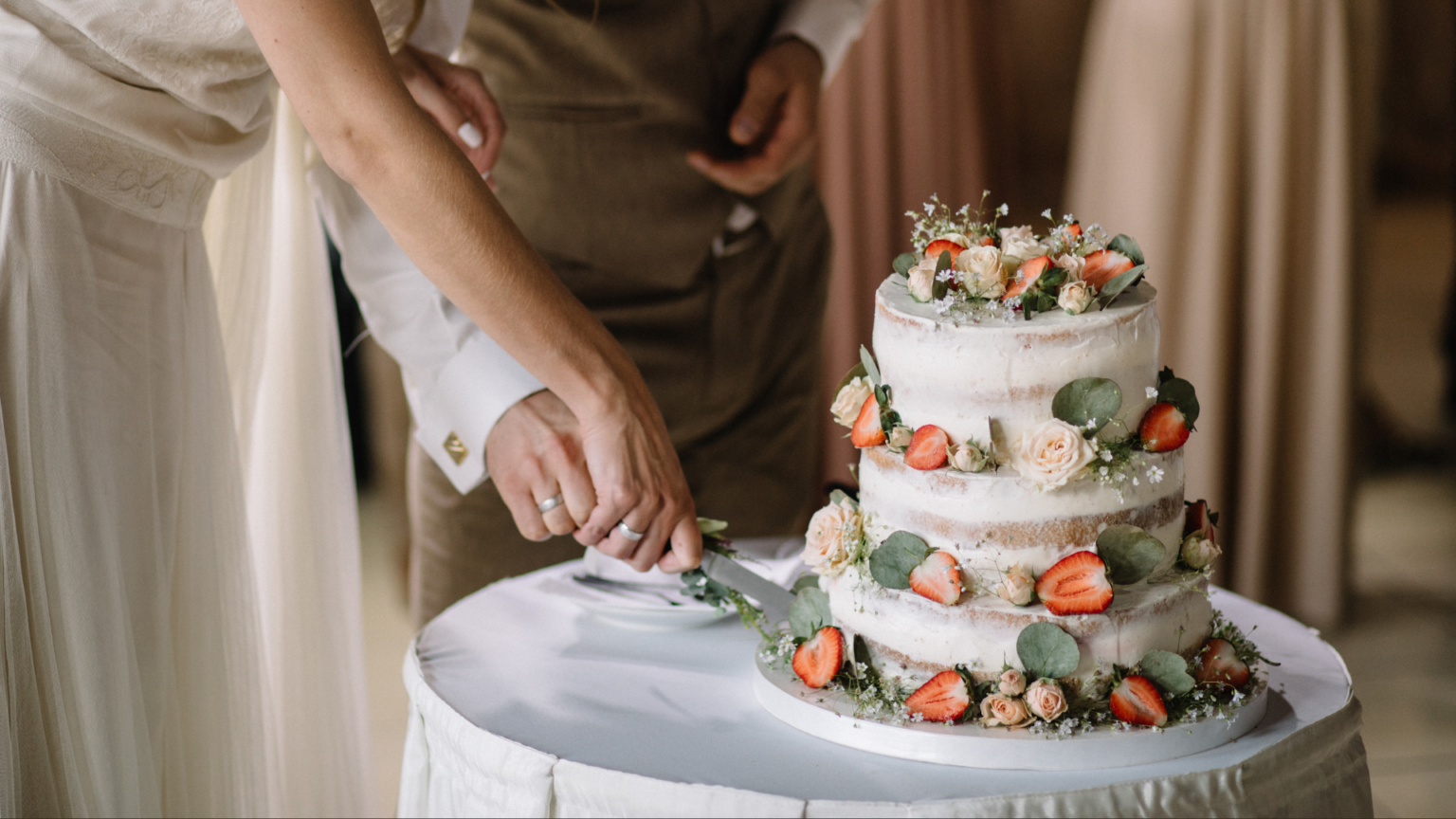 Bride and groom cutting a three-tier wedding cake decorated with strawberries and roses.