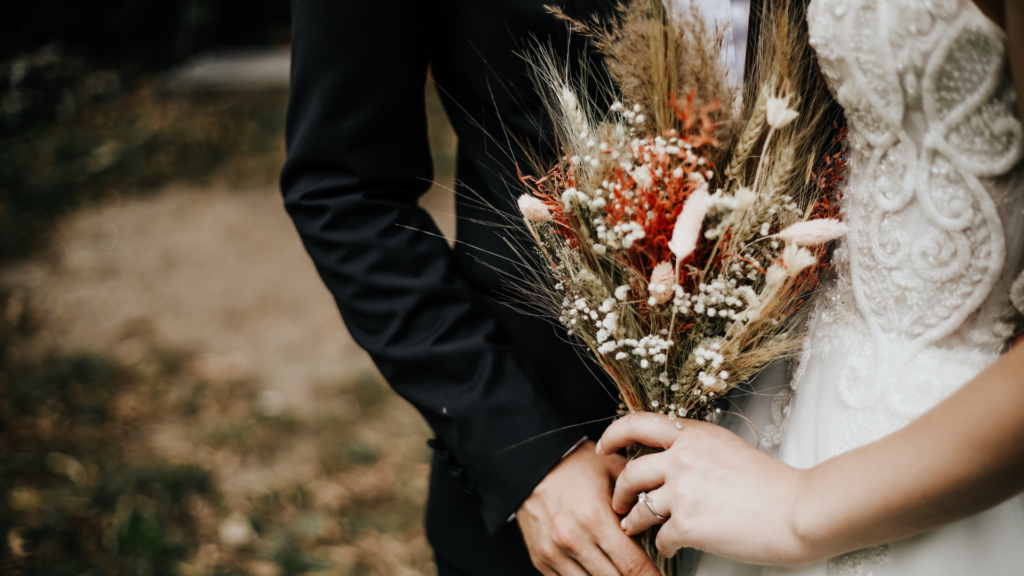 Bride holding dried flower bouquet with groom beside her.